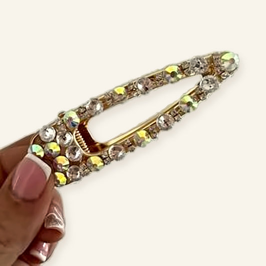 Denoon London crystal hair slide, medium, gold-tone with sparkling clear and iridescent crystals, held in hand on cream