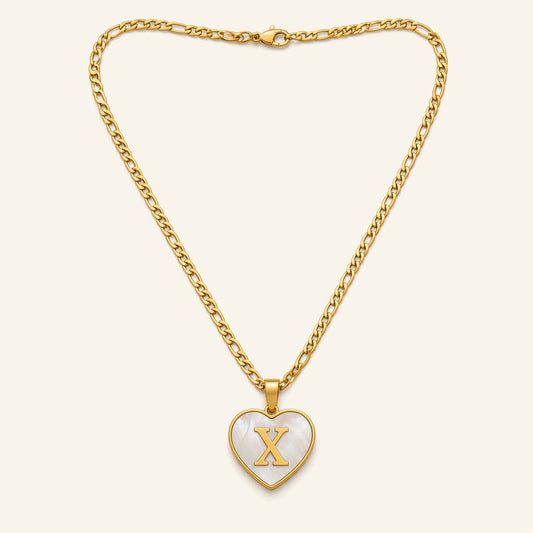 Denoon London initial heart necklace in gold-tone, heart pendant with white inlay and letter X, figaro chain, flat lay on cream