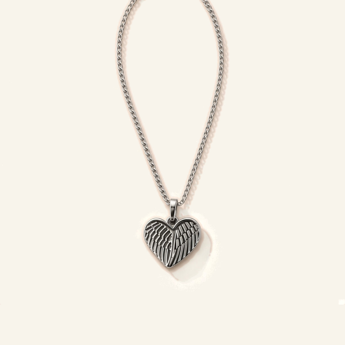 Denoon London Angel Wing Heart necklace in silver-tone stainless steel, 45cm chain, flat lay on cream