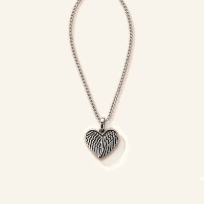 Denoon London Angel Wing Heart necklace in silver-tone stainless steel, 45cm chain, flat lay on cream