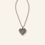 Denoon London Angel Wing Heart necklace in silver-tone stainless steel, 45cm chain, flat lay on cream