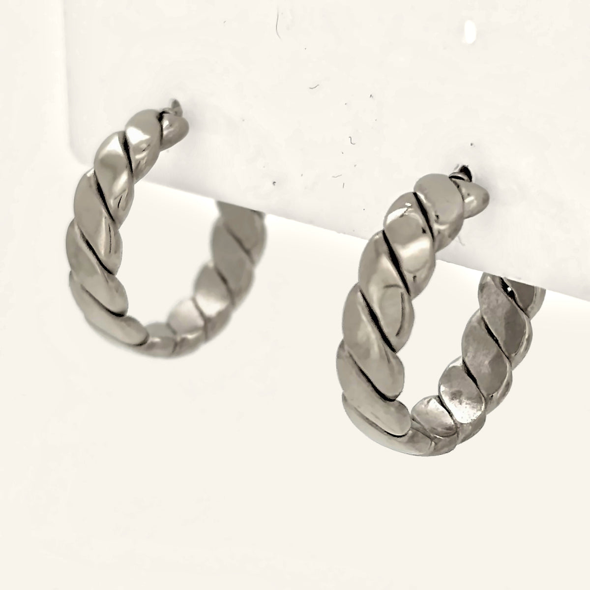 Denoon London chunky twisted hoop earrings, silver-tone, close-up side view on cream