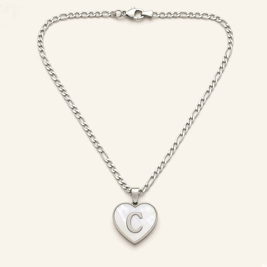 Denoon London initial heart necklace in silver-tone, heart pendant with white inlay and letter C, figaro chain, flat lay on cream