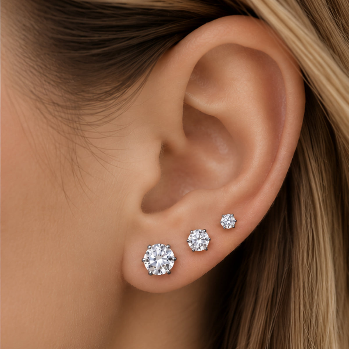Denoon London set of three solitaire stud earrings worn on the ear, shown in silver-tone